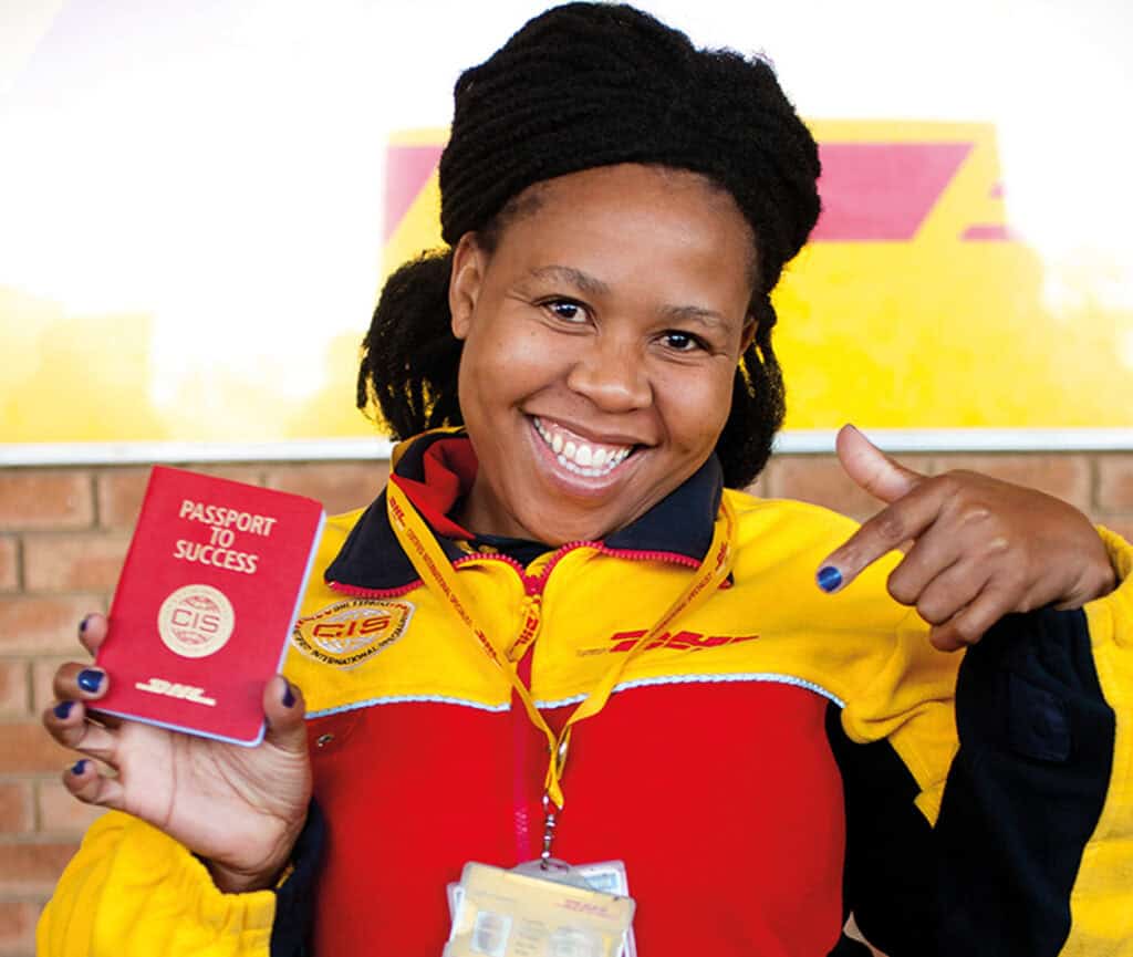 Smiling DHL employee in yellow and red uniform holding a red "Passport to Success" CIS booklet