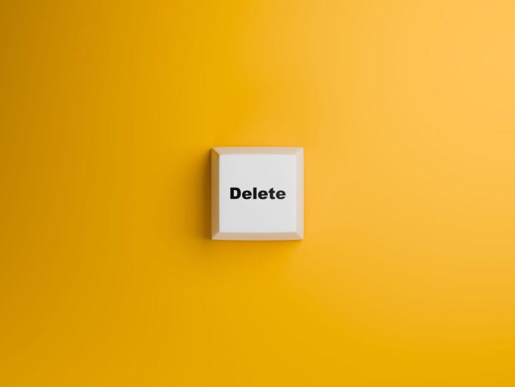 Single white keyboard key marked Delete against a bright yellow wall