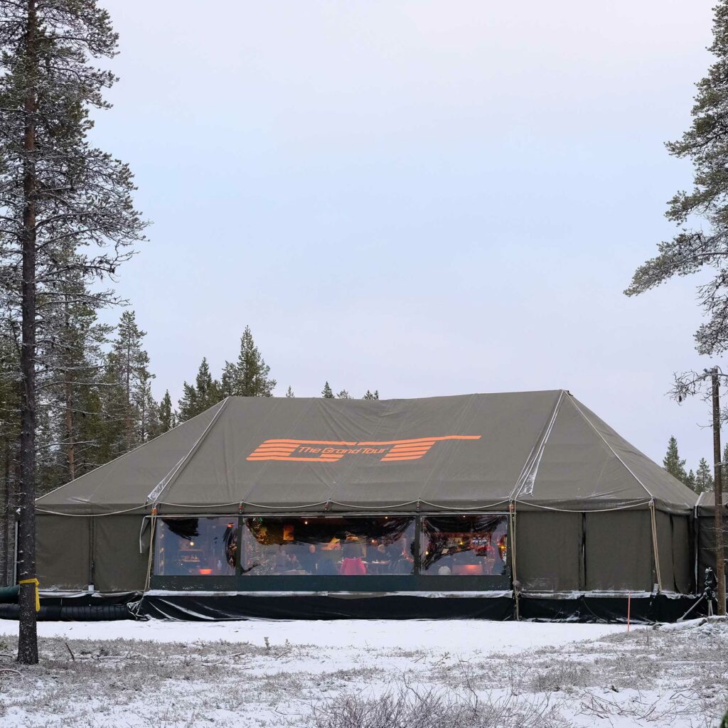 The Grand Tour's tented studio in a snow-covered pine forest, with the orange GT logo across its roof.