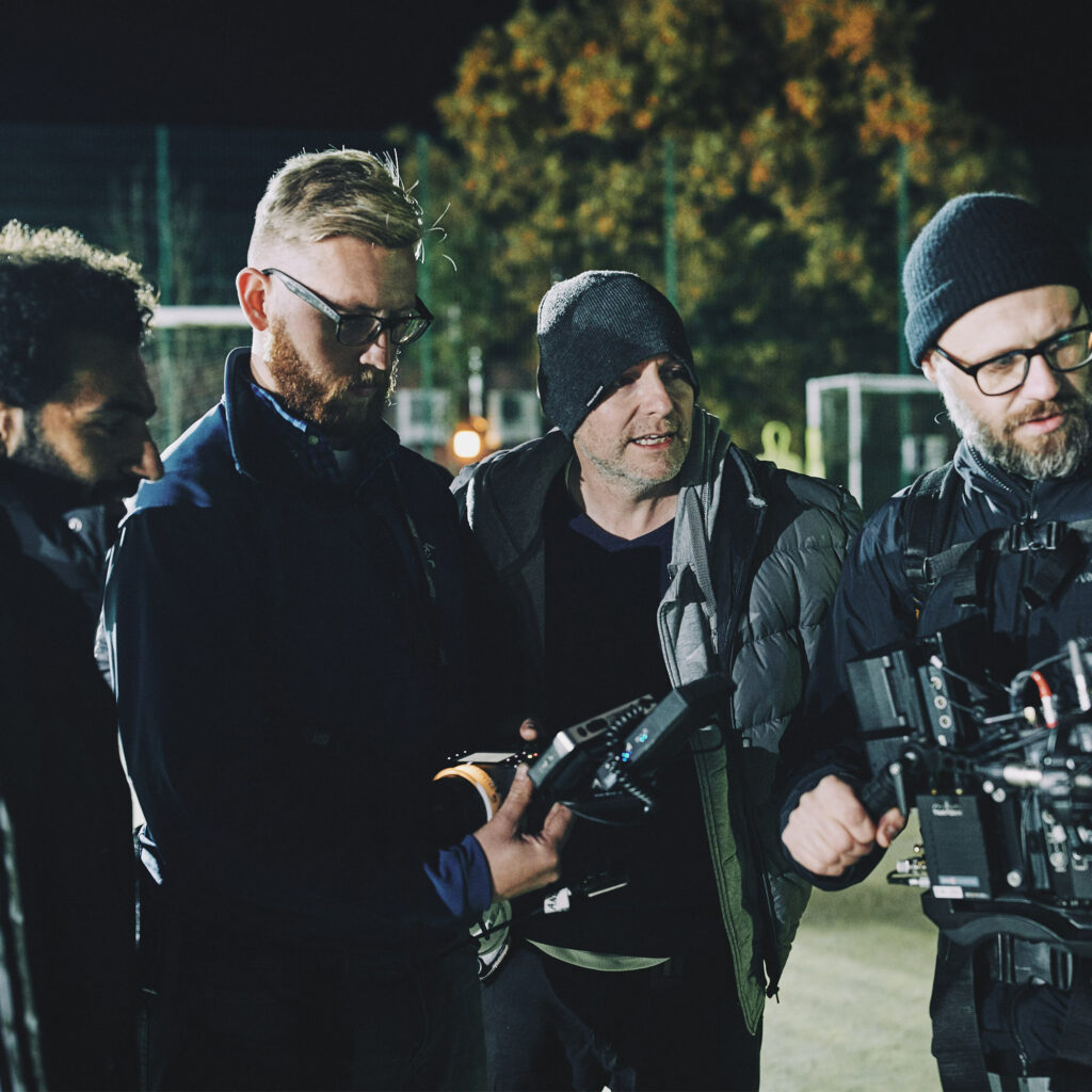 Mo Salah watches playback with the film crew on a floodlit pitch at night during the DHL shoot.