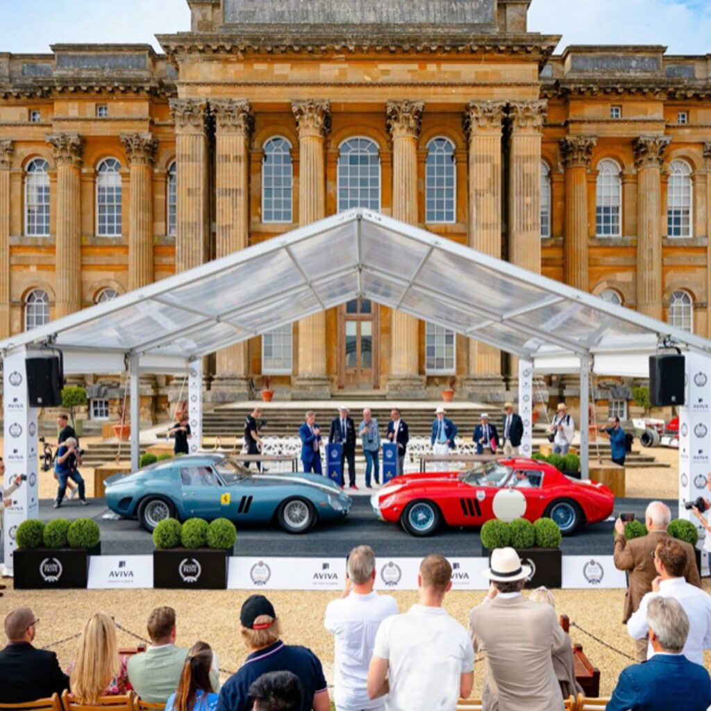 Two classic Ferraris on the concours stage in front of Blenheim Palace, with judges on the podium and a seated audience.
