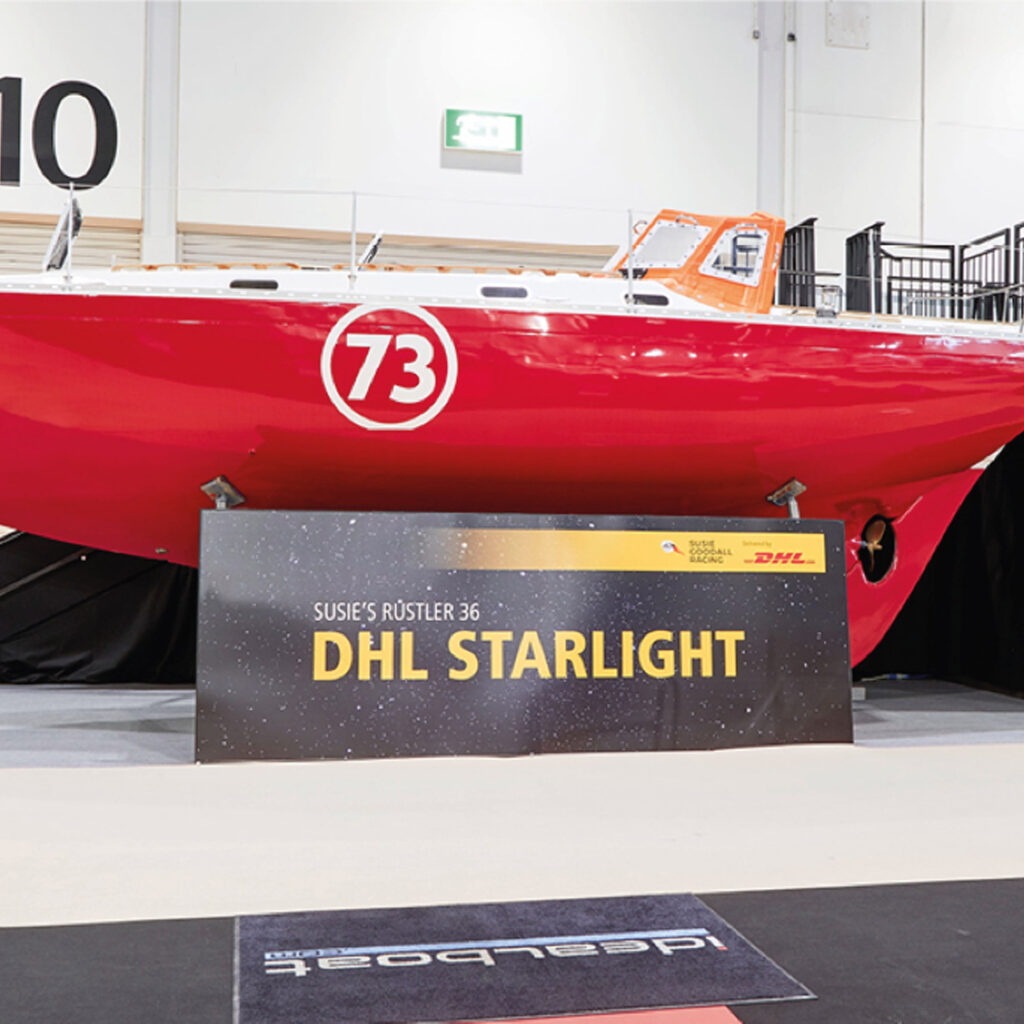 Susie Goodall's red Rustler 36 yacht, number 73, on display indoors beside a board reading "Susie's Rustler 36 DHL Starlight".