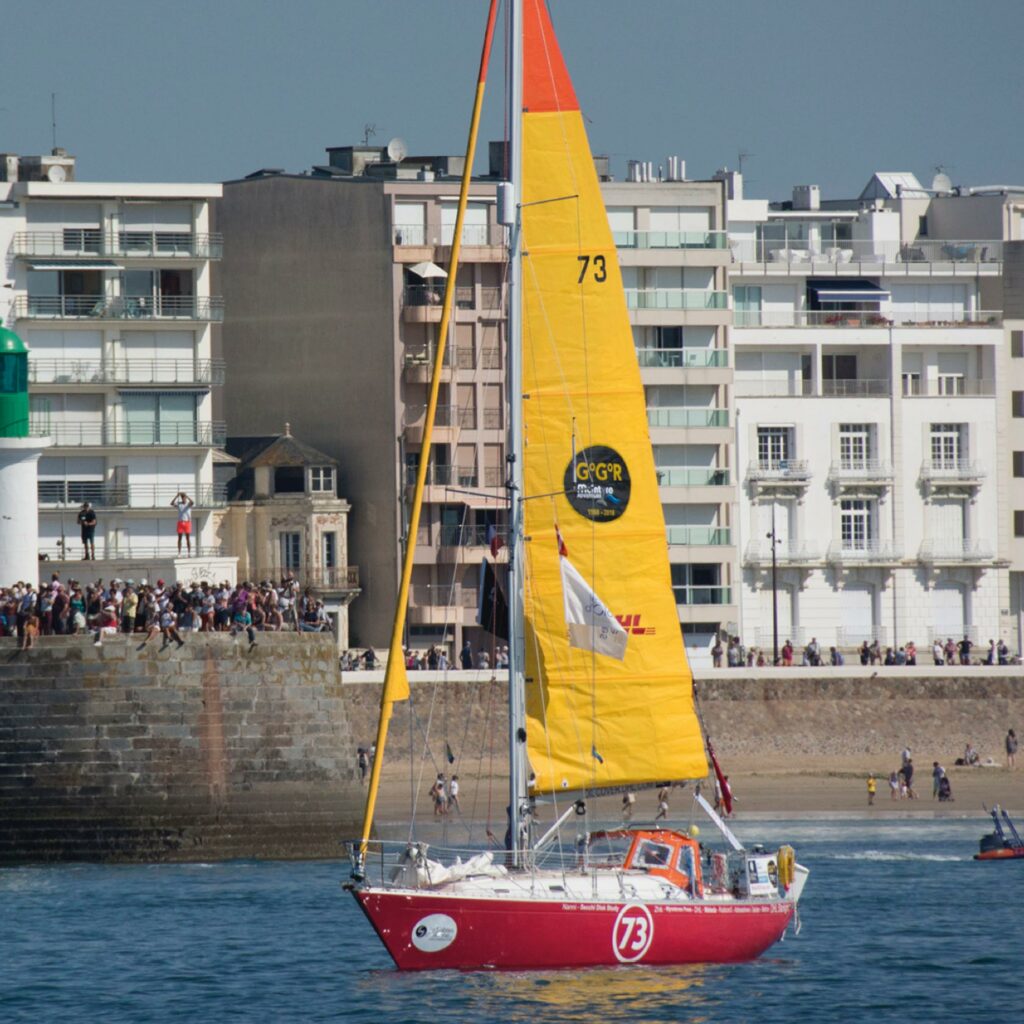 The yacht DHL Starlight under yellow sail, number 73, sailing past a crowded harbour wall of spectators.