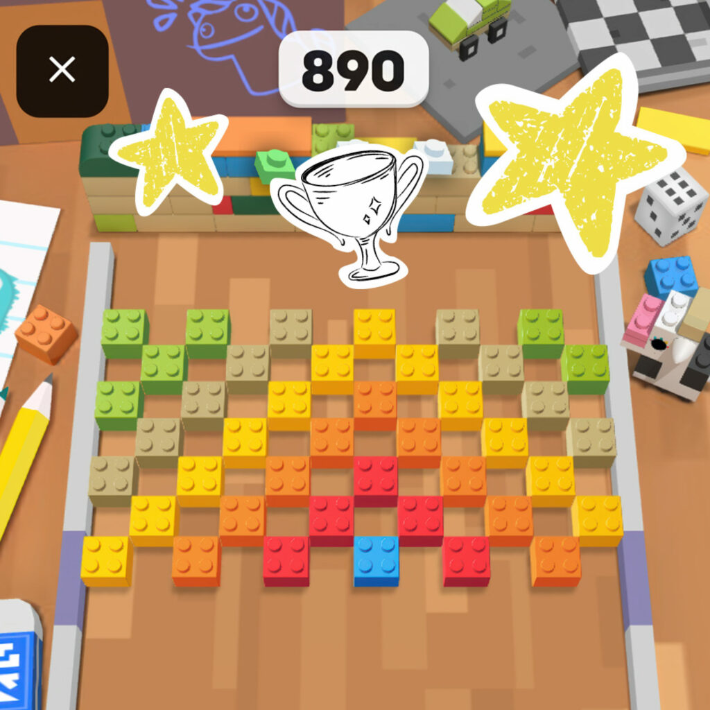 A LEGO brick game board on a desk showing a score of 890, with trophy and star doodles